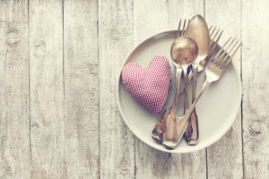 Love, valentine's day or eating concept with vintage cutlery, plate and plush heart on a wooden background. Top view with copy space